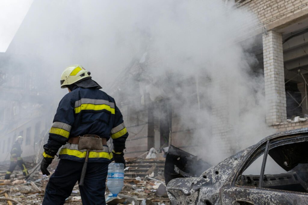 A firefighter in uniform combats a smoky urban disaster scene amidst destruction and debris.